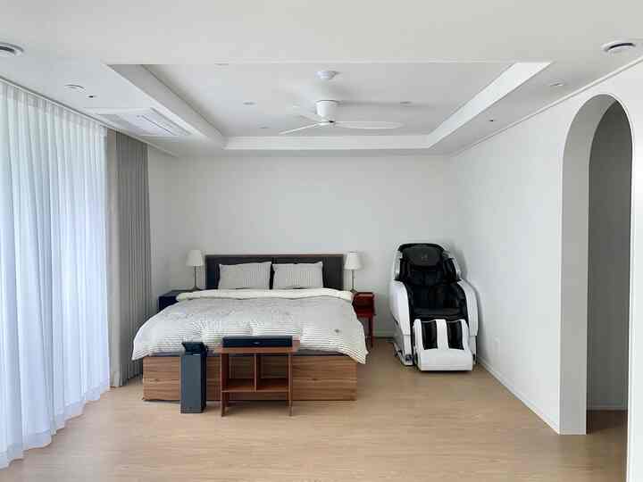 白と木目調の寝室、ベッドとリクライニングチェア、カーテンが配置された清潔で居心地の良いインテリア