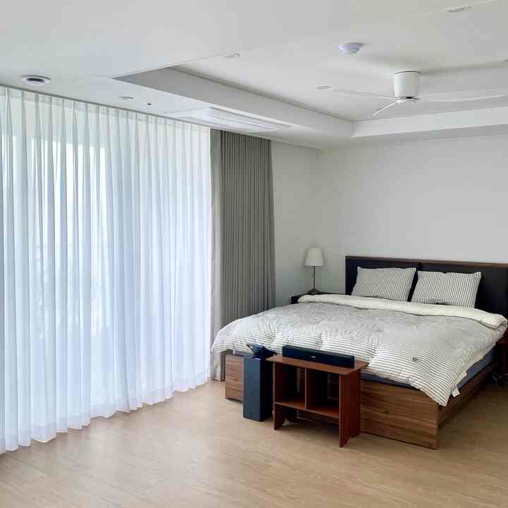 White and natural-toned bedroom featuring a large bed with layered curtains in a clean, modern space