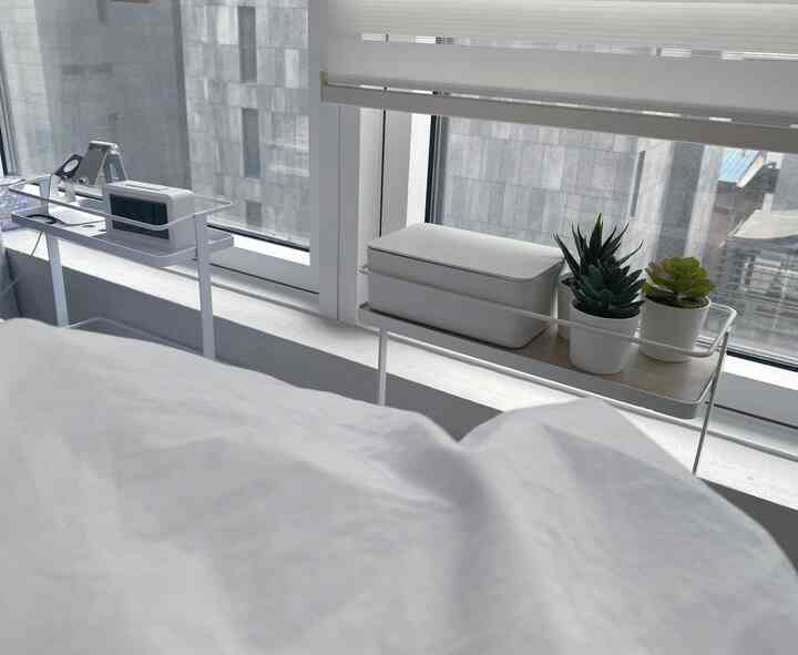White-toned bedroom space featuring narrow gap storage shelves, a digital clock, and small potted succulents creating a simple, natural atmosphere