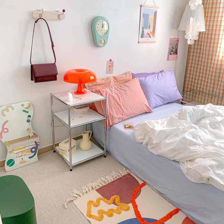 Bright and airy bedroom with pastel pillows, white duvet cover on bed, and a red lamp on the nightstand