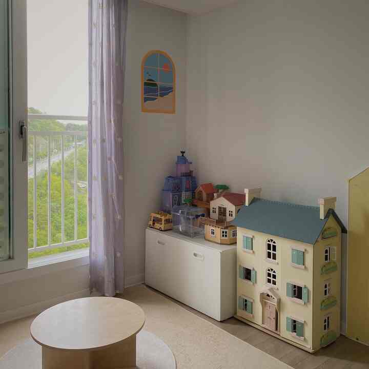 明るいナチュラルトーンの子供部屋、玩具収納と円形テーブル、窓際に紫の花柄カーテンが配置された雰囲気のあるインテリア