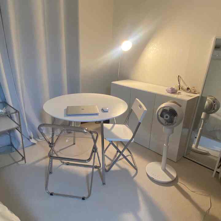 白を基調としたワンルーム空間、丸テーブルと折りたたみ椅子、フロアランプが配置されたシンプルな雰囲気のインテリア