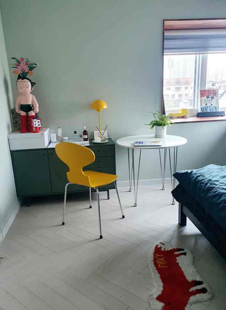 カーキ色のチェストと淡い緑の壁紙、黄色い椅子とランプが置かれた息子の寝室