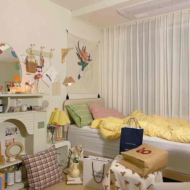 Bright natural-toned bedroom featuring a bed with yellow bedding, sheer white curtains, and a fabric poster with floral illustration on the wall creating a cozy atmosphere