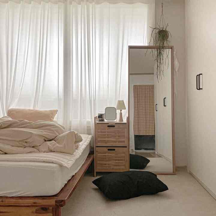 Bright white-toned bedroom featuring a wood-tone bed frame and storage cabinet with a natural modern style
