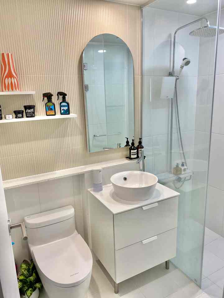 Bright white and beige toned bathroom featuring a cabinet with sink, arched mirror, and a glass shower booth for a clean look