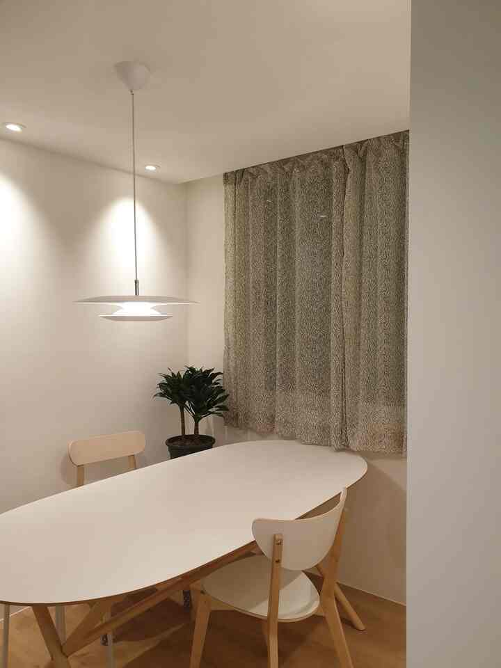 A white and natural toned dining room featuring a white dining table, chairs, patterned curtains, and a green plant with a simple, clean atmosphere