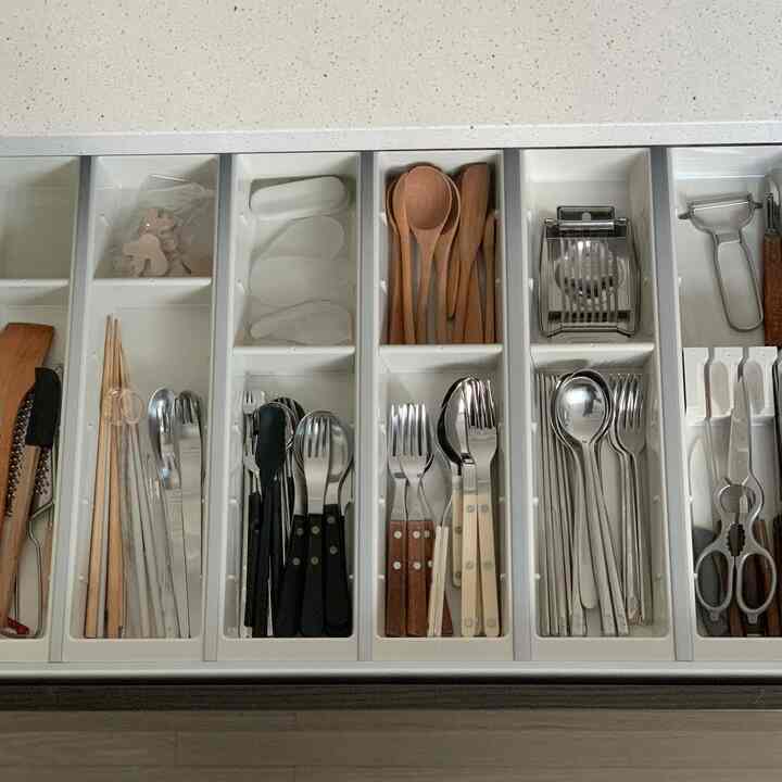 White-toned kitchen drawer featuring organized cutlery and wooden spoons arranged neatly for storage