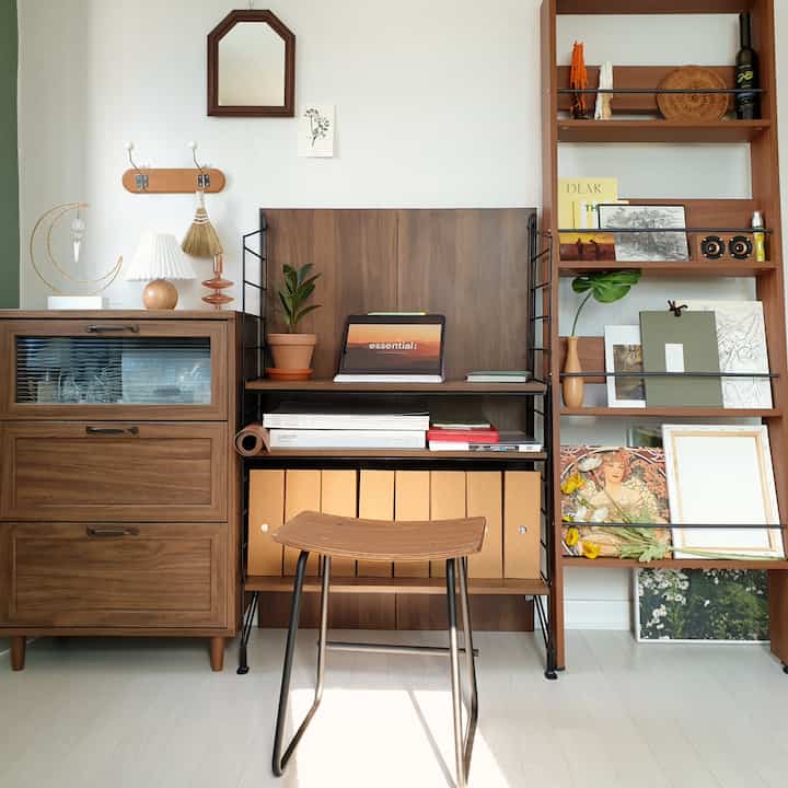 Warm wood tone home office featuring a dresser, magazine rack, and stool arranged for a cozy vintage workspace