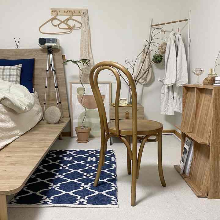 木目調とネイビーの寝室、ラグと木製チェア、本棚が配置された雰囲気のあるナチュラルモダンなインテリア