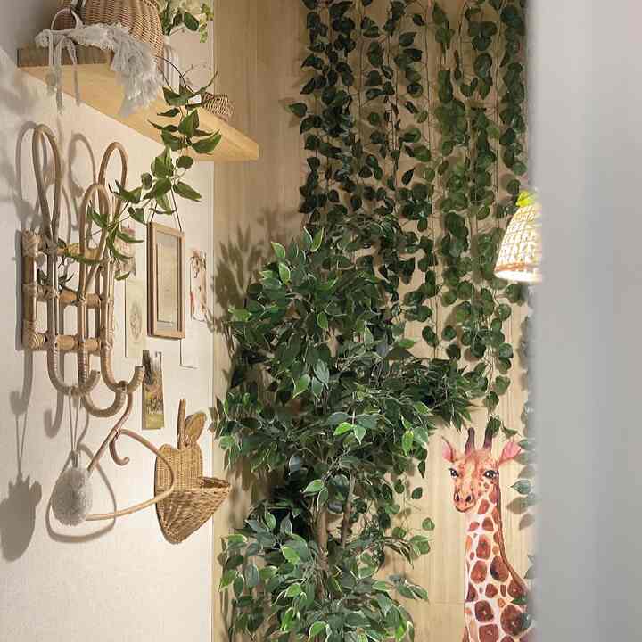 木目調とナチュラル素材が調和する子供部屋の一角、緑の人工植物とラタンの壁掛けが配置された温かみのあるインテリア