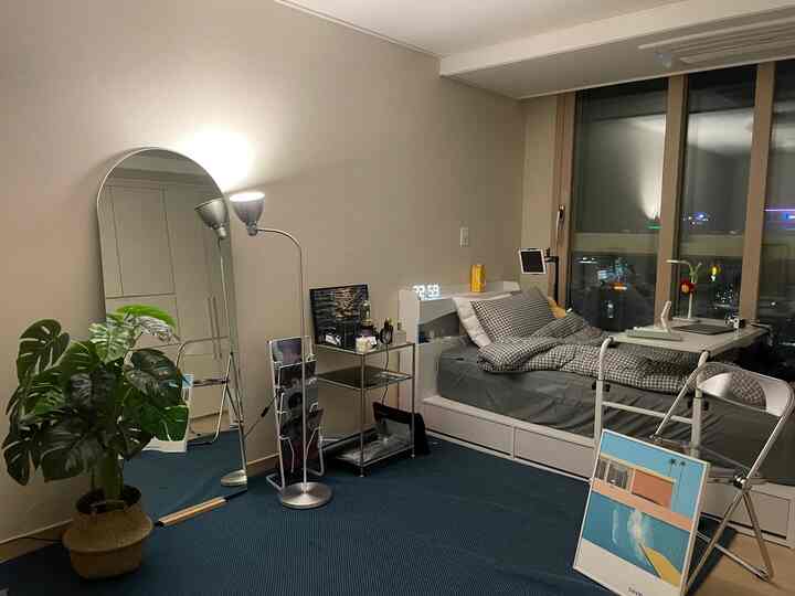A modern studio bedroom in white and gray tones featuring a bed, desk, and floor lamp