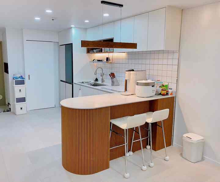 ホワイトとウッドトーンの調和が取れたキッチン、キッチンアイランドとペンダントライトが配置された印象的な空間