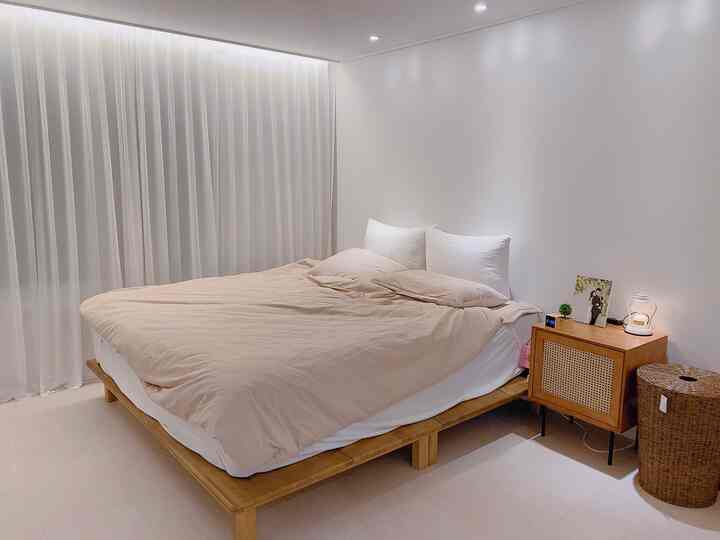 A white and brown toned bedroom featuring a large king-sized bed without headboard and rattan storage, evoking a simple hotel-like style