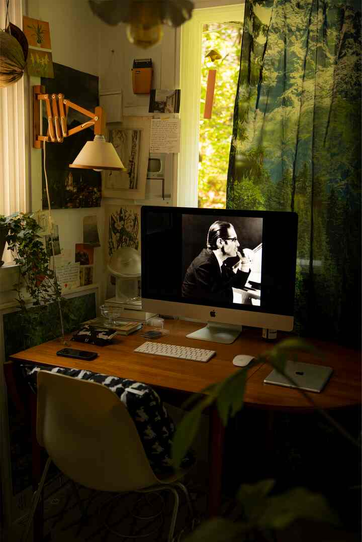 A dark-toned home office featuring a wooden desk and chair, decorative curtains with nature motifs, and a wall-mounted lamp creating a cozy workspace