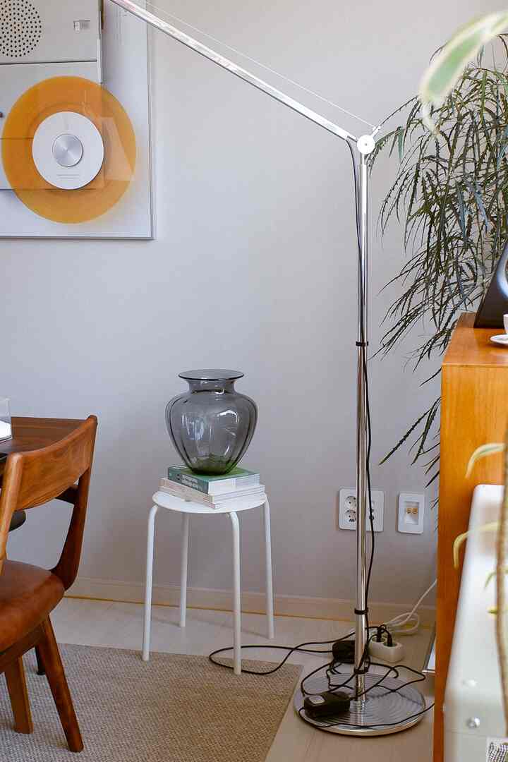 Living room with white walls and wood-tone furniture featuring a vase on a stool and a chrome floor lamp, creating a natural atmosphere