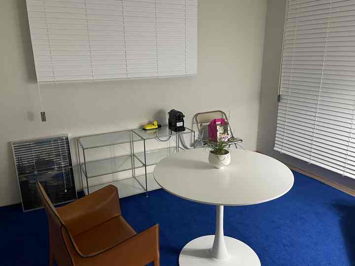 ホワイトとナチュラルカラーの狭い部屋、ブラウンレザーのアームチェアと白い丸テーブル、青いラグが配置されたシンプルモダンなインテリア