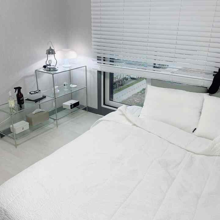 White-tone bedroom featuring a white bed and a sleek stainless steel shelf, creating a simple atmosphere