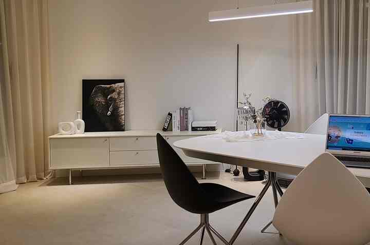 Bright white-toned dining room featuring a white dining table, black dining chairs, and a white TV stand in a modern setting