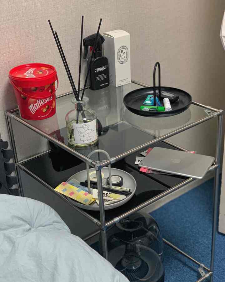 Black glass and metal framed modular shelf holding assorted small household items in a compact practical storage setup