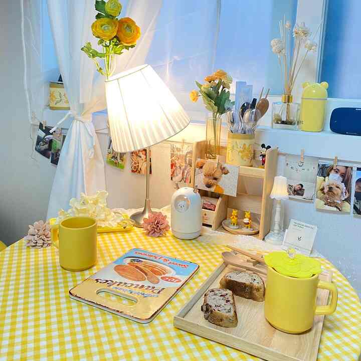 明るい黄色のテーブルクロスとマグカップが置かれたアットホームなおうちカフェ、ペットの写真とテーブルランプが配置された雰囲気のあるインテリア
