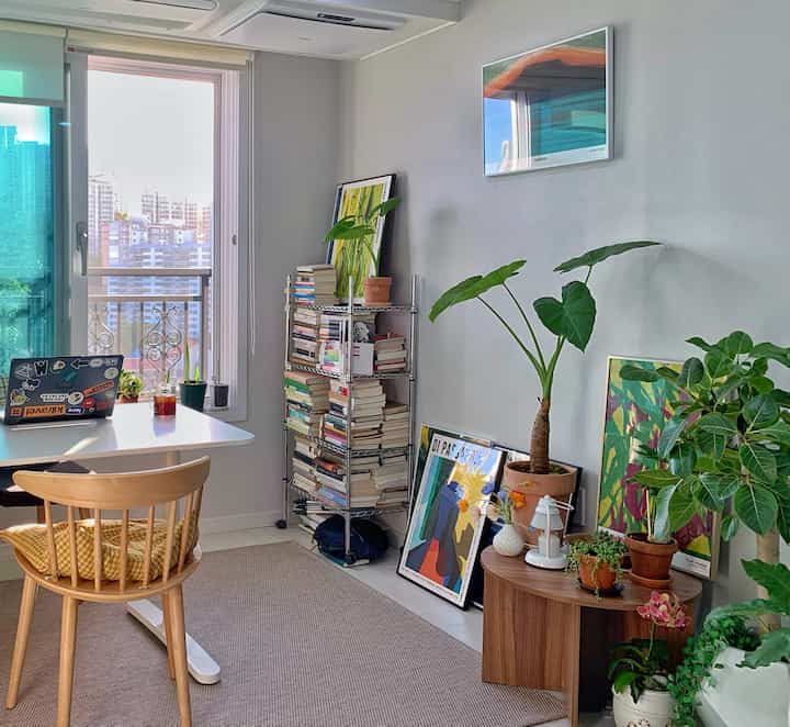 Bright white and wood-toned compact workspace and living room featuring plants and framed art with a cozy atmosphere