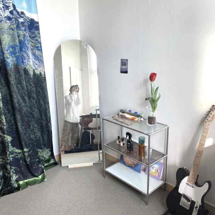 白とグレーのトーンのワンルーム、アーチ型の鏡とモジュール家具、カーテン、ギターが配置されたシンプルでモダンなインテリア