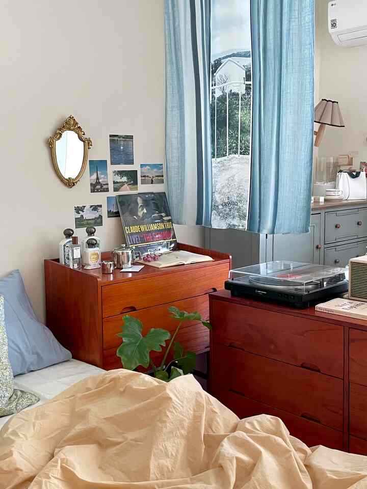 木目調と青いカーテンが調和する寝室、ヴィンテージの装飾とチェストが配置された雰囲気のあるインテリア