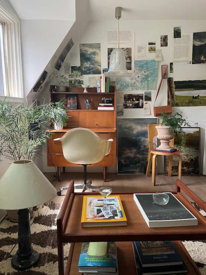 白い壁と木目調家具が調和したホームオフィス兼書斎、机や植物、額縁が配置された落ち着いた作業空間