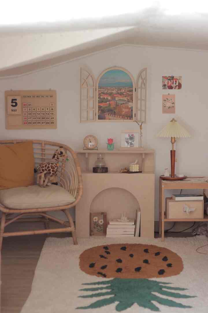 White-walled loft space with wood tone furniture, featuring a rattan armchair, perpetual calendar, stand lamp, and arched poster creating a cozy atmosphere