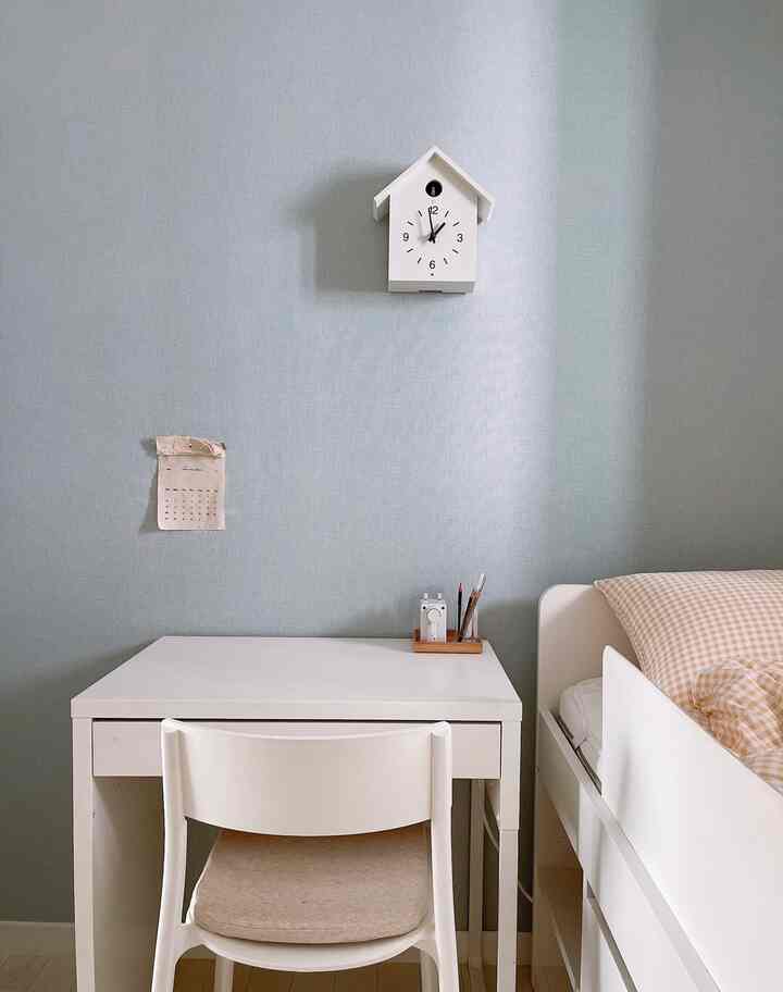 A soft blue-walled kids' room featuring white furniture including a desk, chair, and bed, arranged with a simple and natural atmosphere