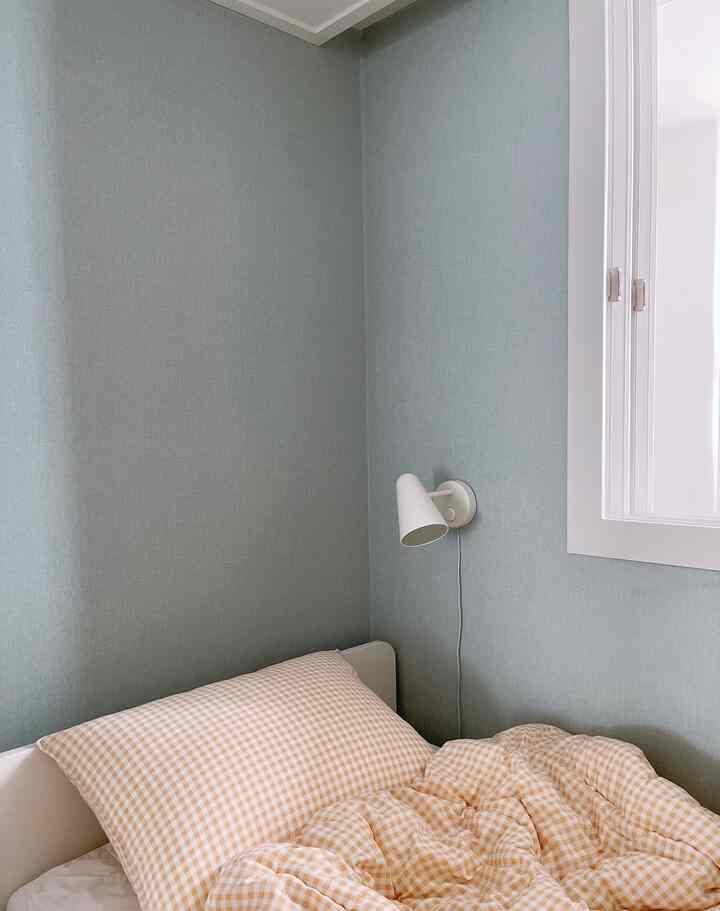 Cozy bedroom corner with soft beige bedding, white bed frame, and light blue-toned walls