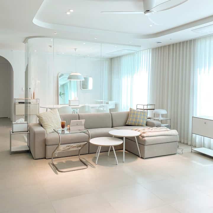 明るいホワイトトーンのリビング、広いガラスパーティションとモダンなソファ、丸テーブルが配された落ち着いたナチュラルモダンのインテリア