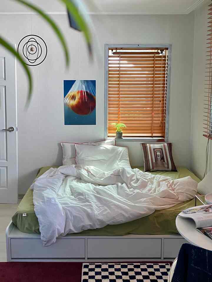 White and wood tone bedroom featuring a storage bed and wood blinds, creating a neat and natural atmosphere