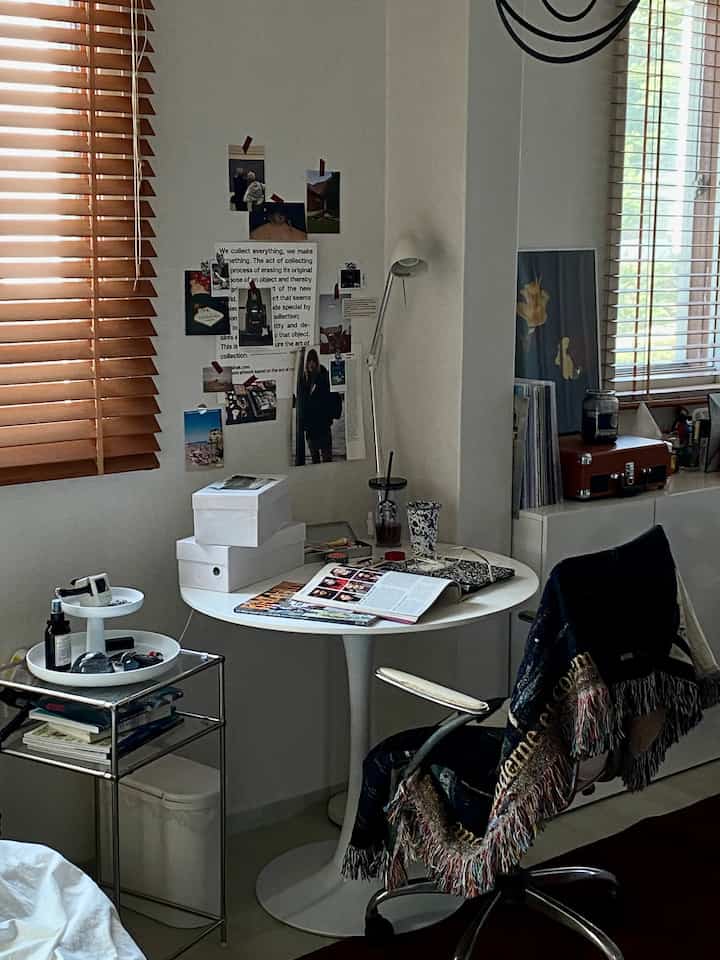 白とウッドトーンのワンルーム作業スペース、丸い机と椅子、壁のポスターが特徴の落ち着いた雰囲気のインテリア