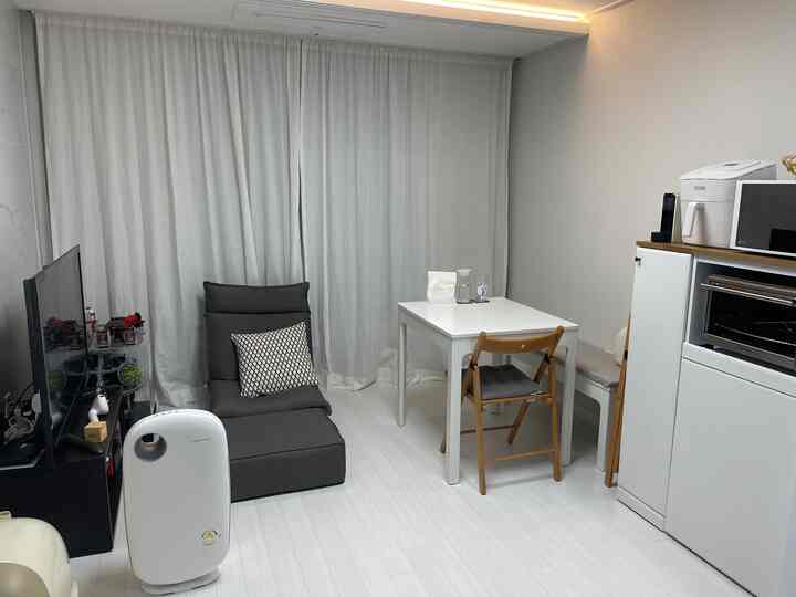 A compact studio apartment with white and gray tones featuring a single sofa and dining table in a minimalistic layout