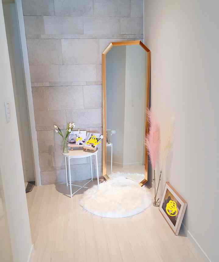 Entrance space in white and beige tones featuring gold-framed full-length mirror, white side table, soft rug, and pink pampas grass with a natural vibe