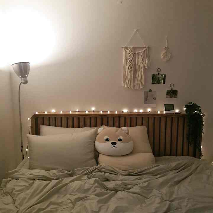 Natural-toned bedroom featuring wooden headboard, beige bedding, dog face cushion, and string lights creating a cozy atmosphere