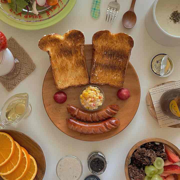 Natural wood tone round plate with bear-shaped toast, sausages, and corn salad styled as cute food for a child on a home cafe table setup
