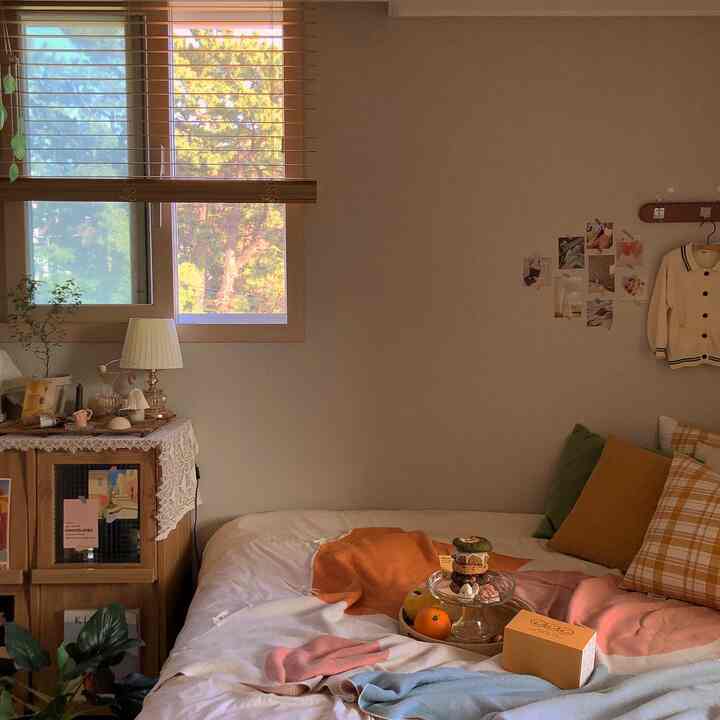 A cozy bedroom with warm wood tones and beige hues featuring a coat rack with clothes and postcards as decoration