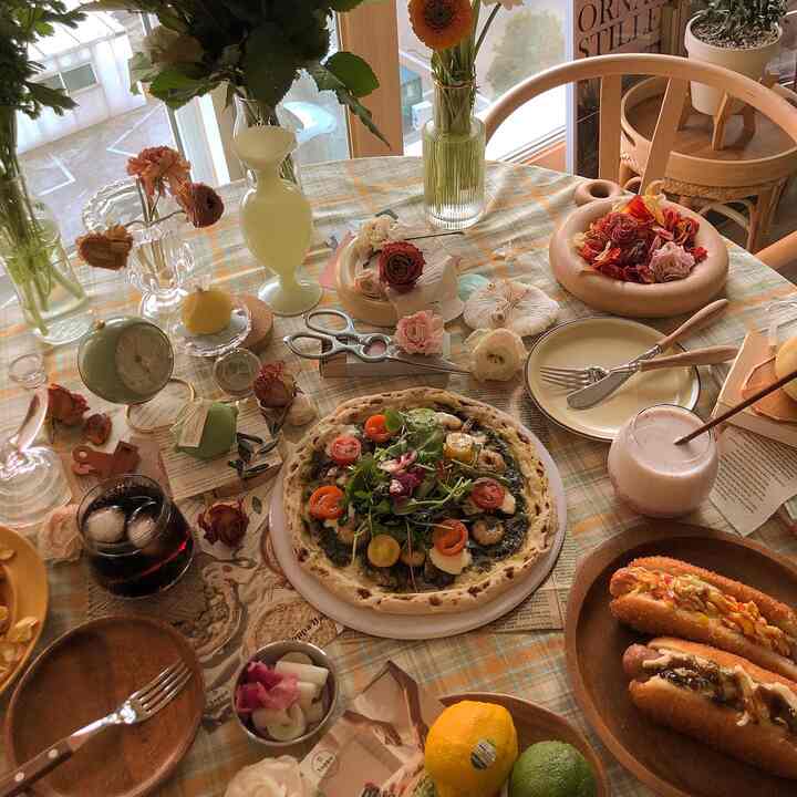 ブラウンとナチュラルな色調のダイニングルーム、円形テーブルにテーブルクロスと花瓶、ピザやドリンクが置かれた雰囲気のあるホームカフェインテリア