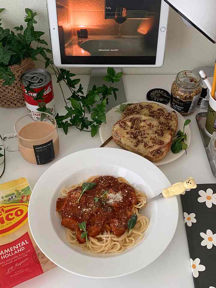白を基調とした小さな部屋のデスク、グリーンプラントが配され、パスタボウルと飲み物がある雰囲気のあるインテリア