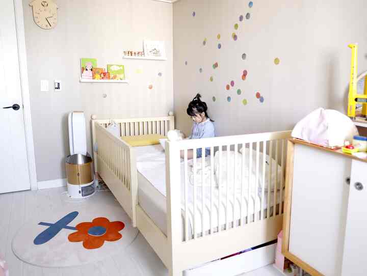White and yellow toned kids' room featuring a crib bed, wall clock, and round rug creating a bright and cozy atmosphere