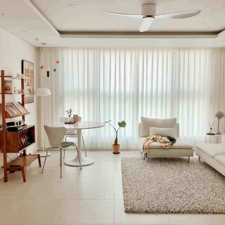 ホワイトとナチュラル色調のリビングルーム、カーテン、大きな窓に白いソファと丸テーブルが配置されたシンプルな印象的な空間