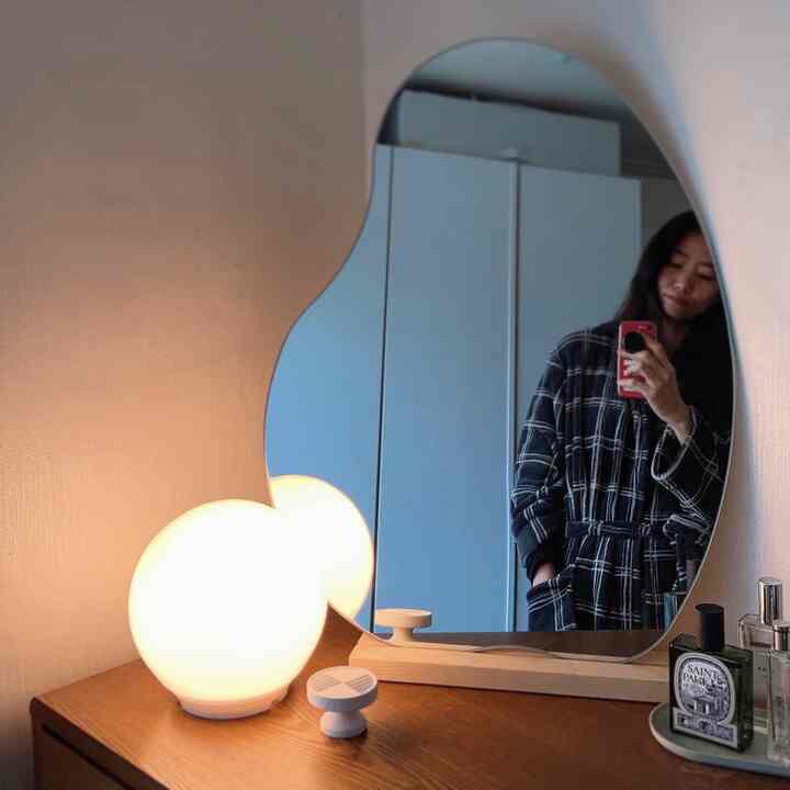 Warm wood tones and white hues in a walk-in closet featuring an irregular-shaped mirror and spherical lamp in a simple, cozy setting