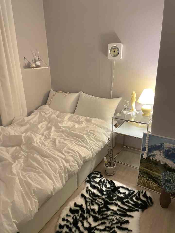 Ivory and white toned bedroom featuring a tidy bed, silver side table, and soft lighting creating a cozy atmosphere