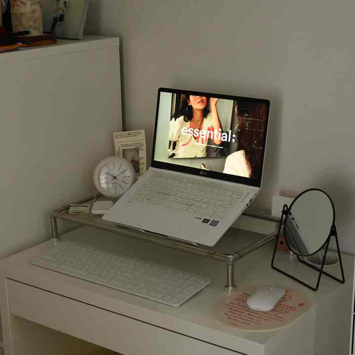 White-toned compact modern home office space featuring a desk with laptop, clock, and mirror arranged neatly