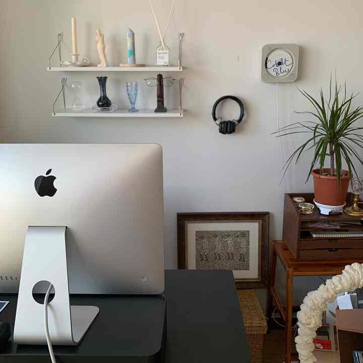 Modern home office with white walls and shelves, sleek desk with iMac, headphones on wall, and potted plant for warmth