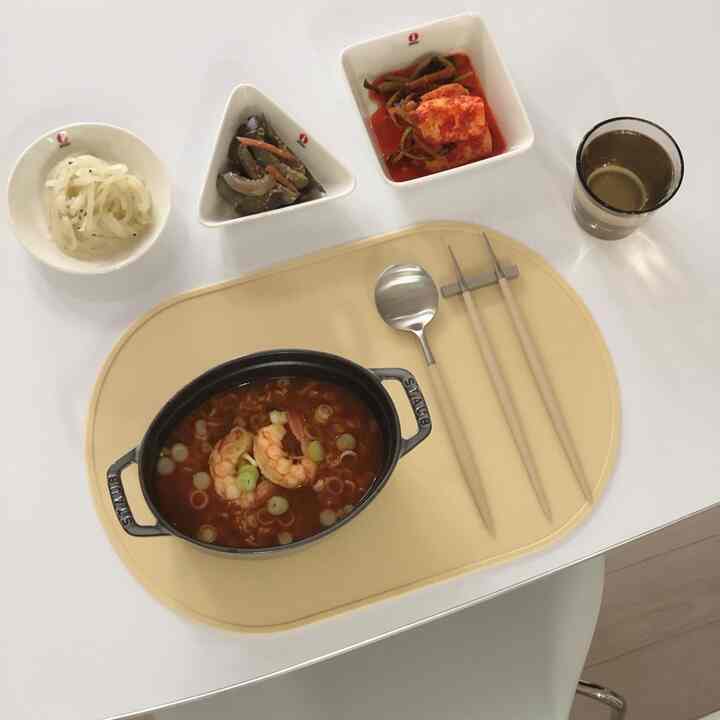 Yellow-toned silicone placemat on a clean dining table featuring a cast iron pot with ramen, three small bowls, and cutlery set