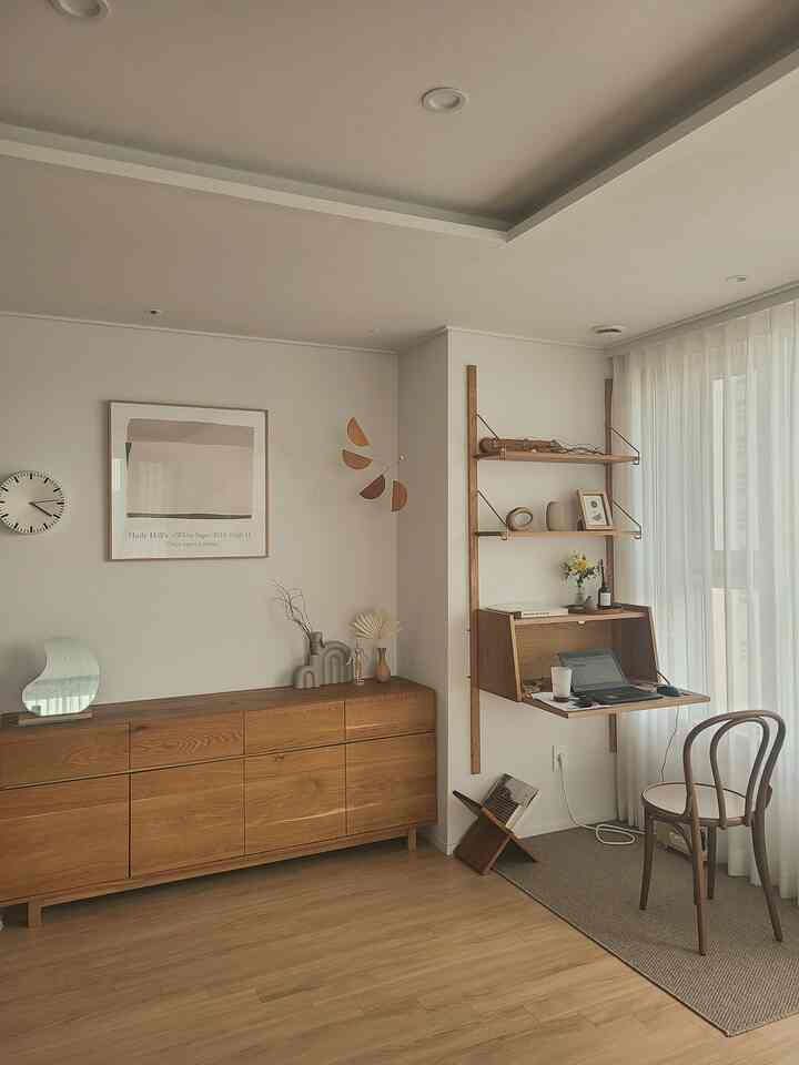 White walls and ceiling with wood tone furniture and wall-mounted desk in a studio apartment home office space